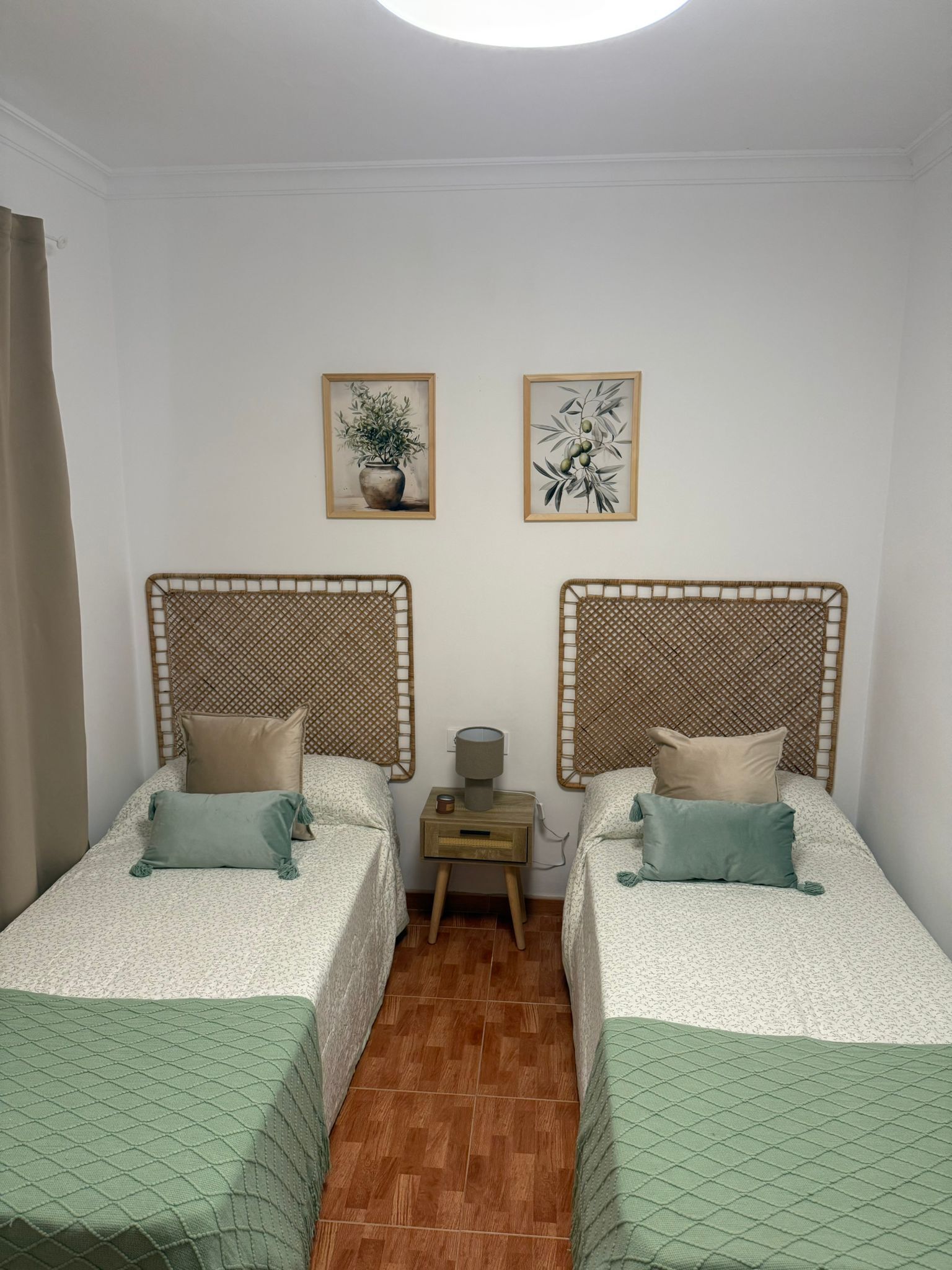 Une chambre avec deux lits, une petite table avec une lampe et deux tableaux encadrés au mur.