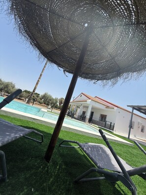 A poolside area with lounge chairs, a pergola, and a white building with a red roof. - Rural lodging los pozos 40 minutes from sevilla (Urbanización Santa Elo)