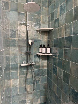 A shower with a handheld showerhead, a handheld showerhead, and a wall-mounted shelf with two bottles of shampoo and conditioner.