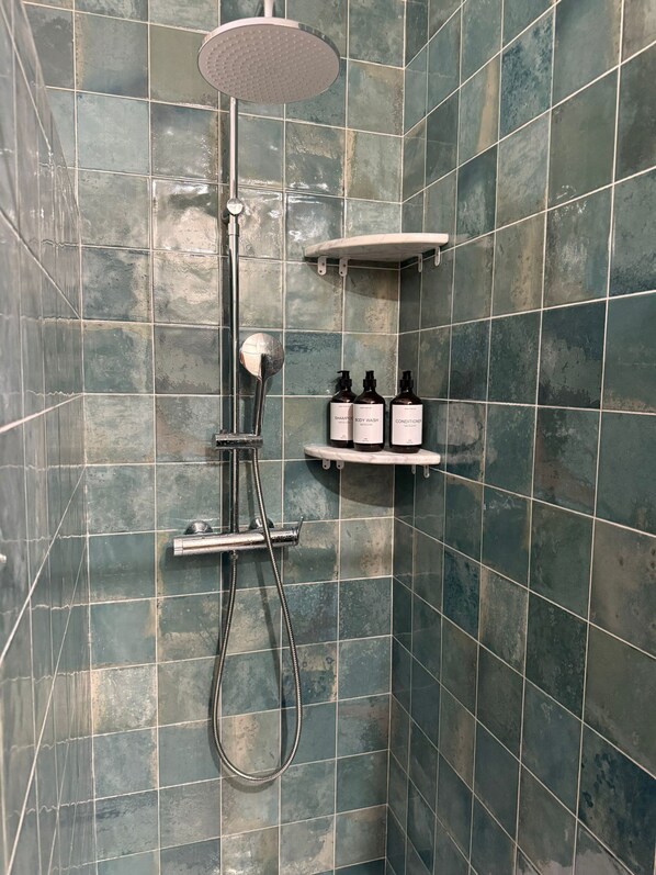 A shower with a handheld showerhead, a handheld showerhead, and a wall-mounted shelf with two bottles of shampoo and conditioner.