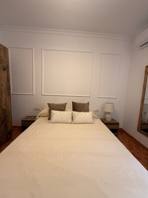 A bedroom with a large bed, two bedside tables, a nightstand, a mirror, and a wooden door.