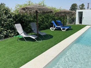 A pool area with artificial grass, two lounge chairs, and a thatched umbrella. - Rural lodging los pozos 40 minutes from sevilla (Urbanización Santa Elo)