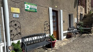 Un bâtiment à la façade en pierre, avec un banc, des plantes en pot et un panneau indiquant qu’il est possible d’y réserver une place.