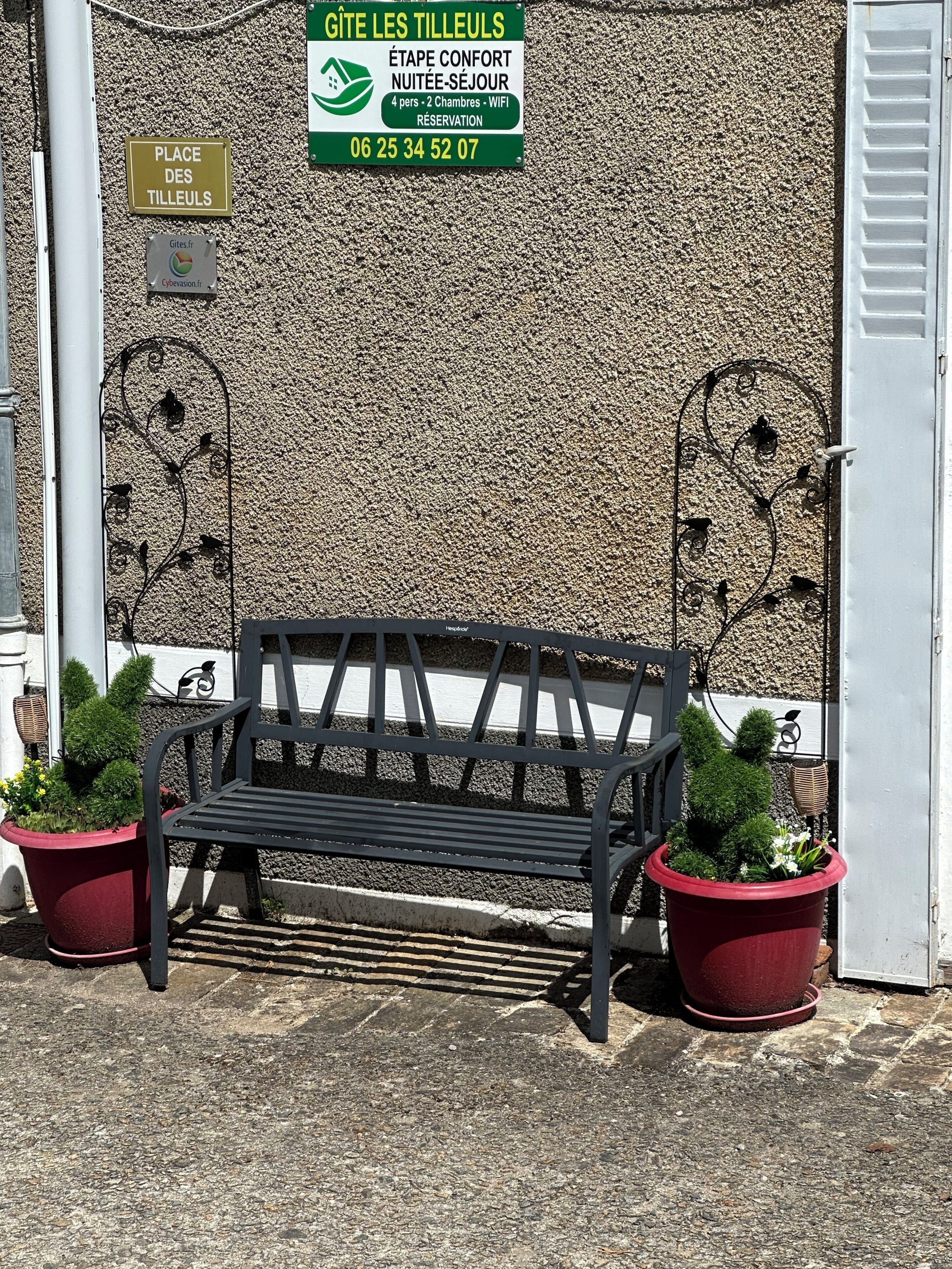 A bench with two potted plants, a textured wall, and a sign indicating a 4-person, 2-bedroom accommodation with WiFi.