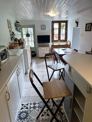 A compact kitchen with a dining area, a television, and a window with a view. - Gîte les Tilleuls, 2-bedroom house with all comforts (Lesterps)