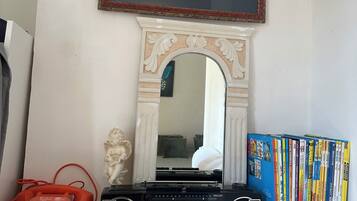 A room with a framed black and white photo, a mirror, a red telephone, a radio, and a bookshelf.