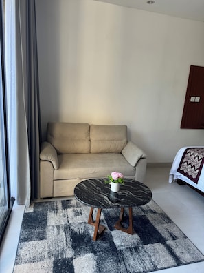 Una stanza con un divano beige, un tavolino nero rotondo e un tappeto decorato.