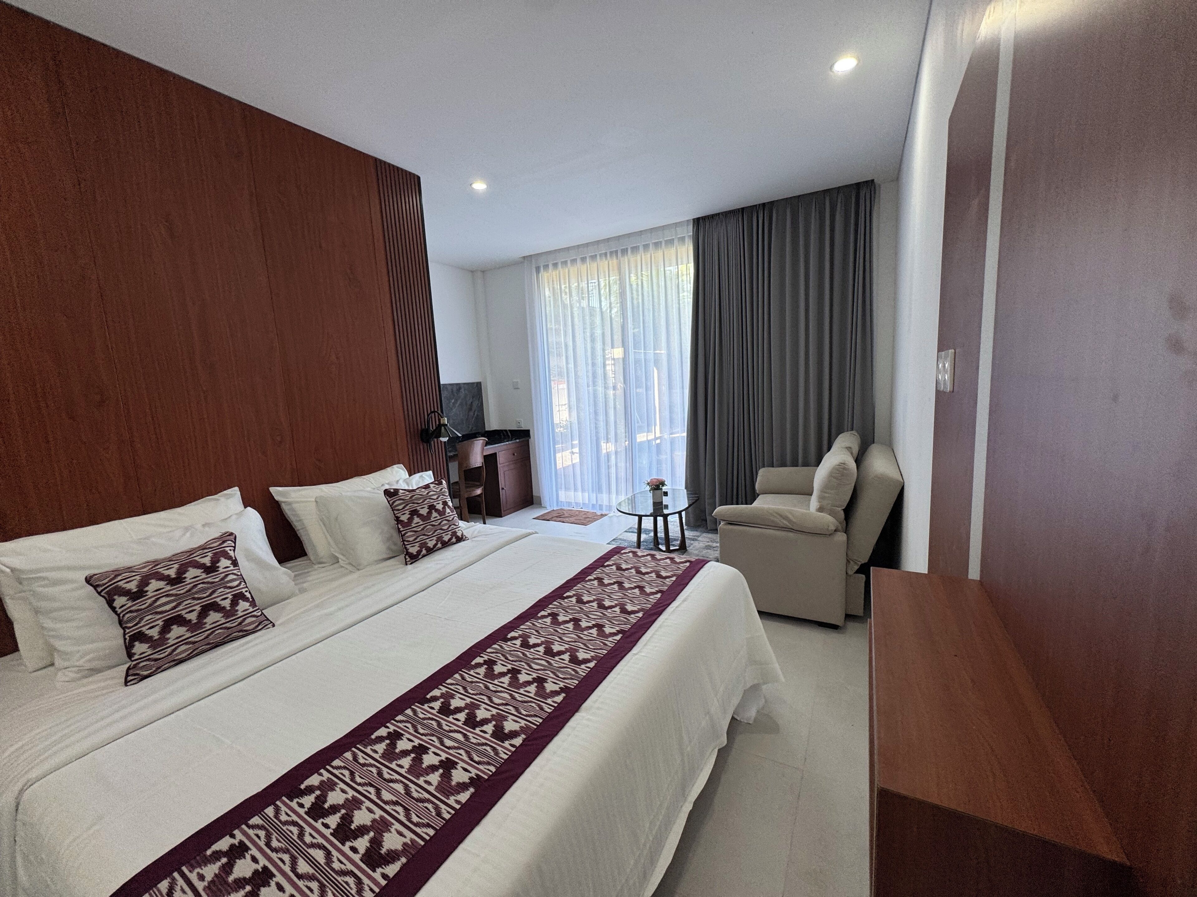 A hotel room with a large bed, a desk, a chair, and a view of the outdoors.