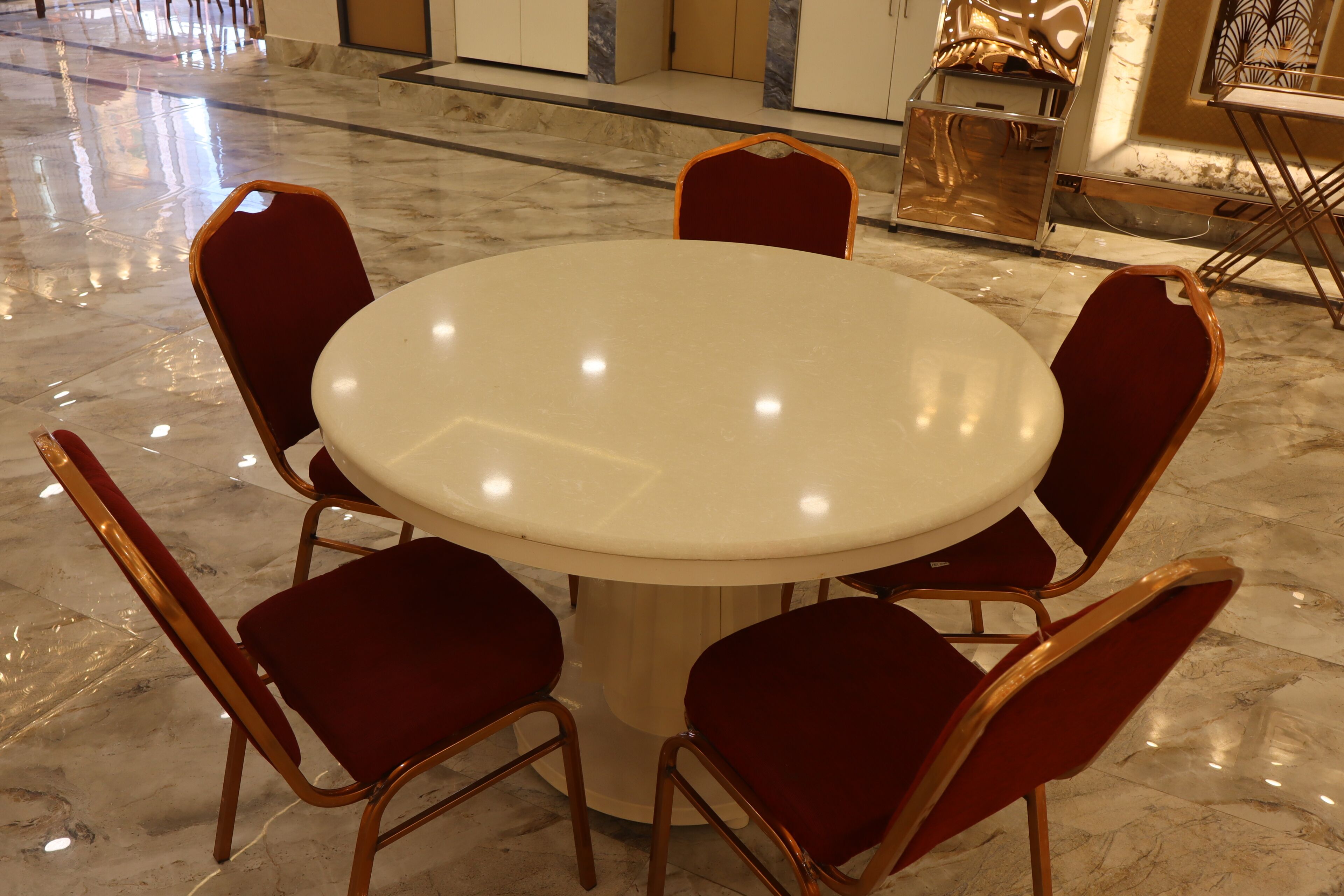 Una mesa redonda con seis sillas tapizadas en rojo en una habitación con suelo de mármol pulido.
