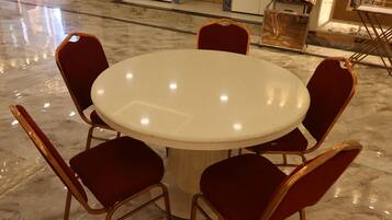 Una mesa redonda con seis sillas tapizadas en rojo en una habitación con suelo de mármol pulido.