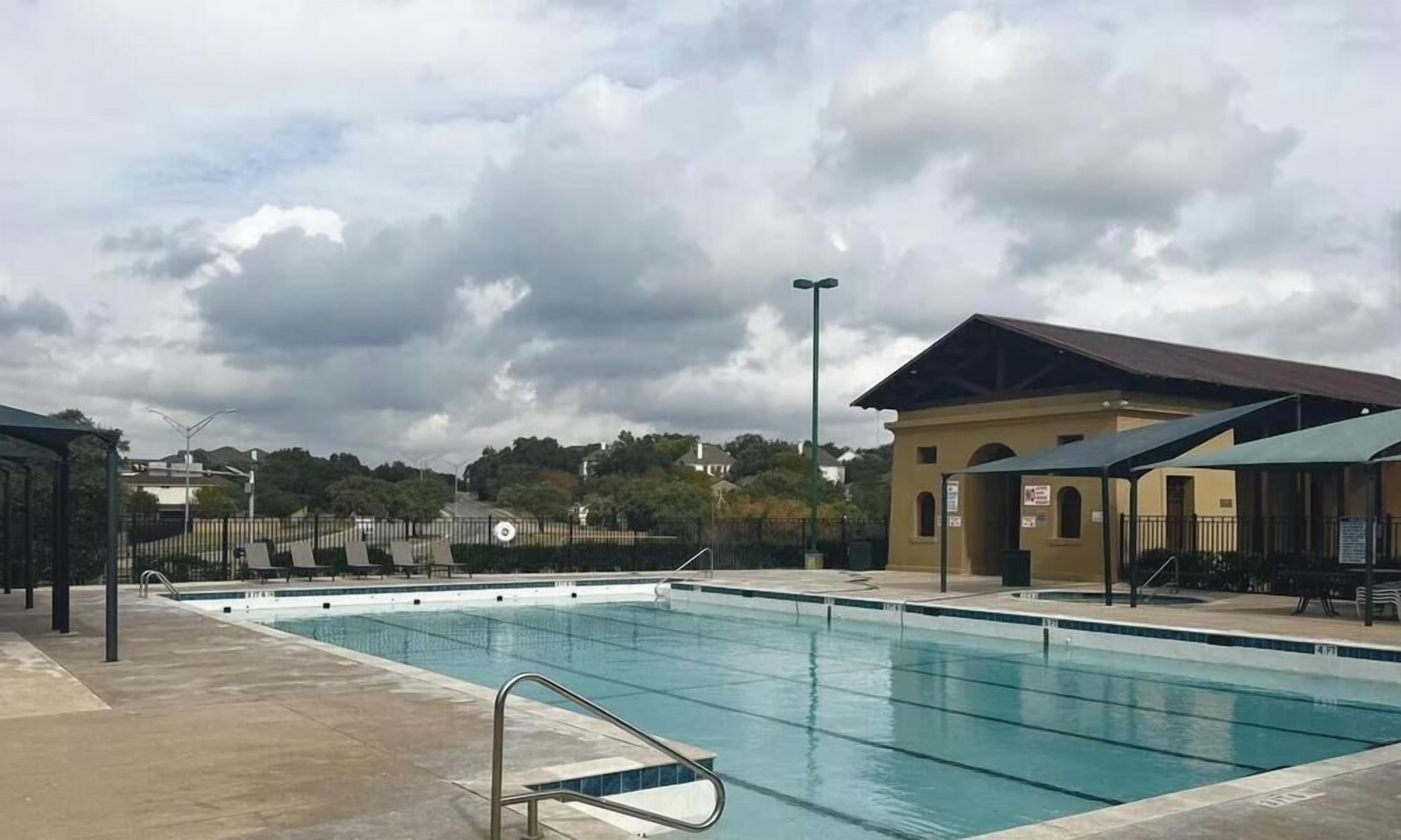 Une piscine avec un escalier en métal, entourée d’une clôture, et un bâtiment avec un toit en pente en arrière-plan.