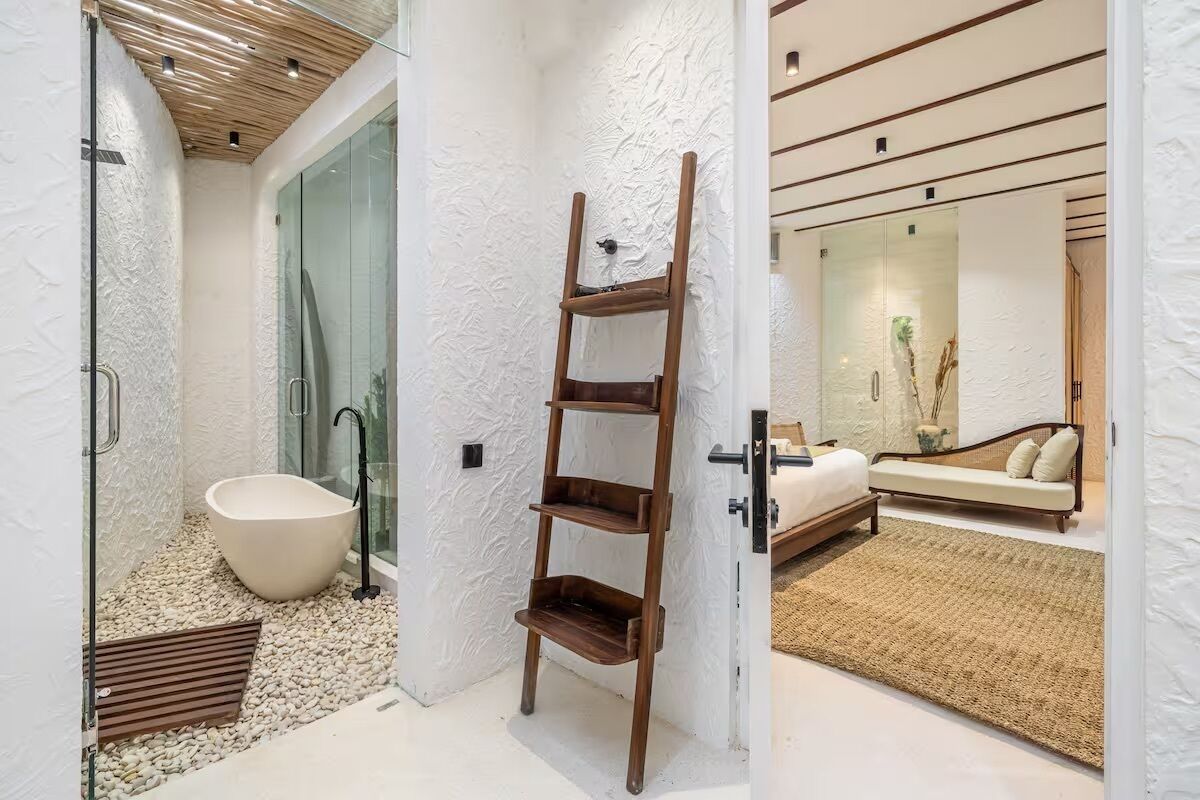 A modern bathroom with a freestanding bathtub, a wooden ladder shelf, and a glass shower enclosure.