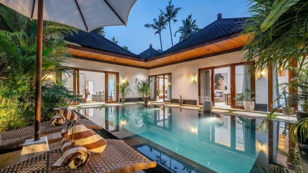 An indoor swimming pool with lounge chairs, surrounded by palm trees and a covered area with wooden beams. - Harmony Villa by DH (Gianyar)