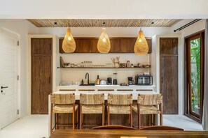 A kitchen with a central island, wooden cabinets, and hanging light fixtures. - Harmony Villa by DH (Gianyar)
