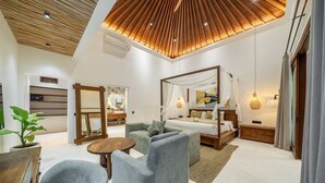 A modern bedroom with a four-poster bed, a sofa, a small round table, and a potted plant. - Harmony Villa by DH (Gianyar)
