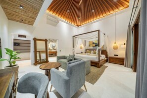 A modern bedroom with a four-poster bed, a sofa, a small round table, and a potted plant. - Harmony Villa by DH (Gianyar)