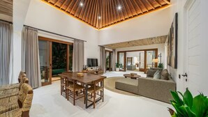 A spacious living area with a wooden ceiling, a dining table, a sofa, and a TV. - Harmony Villa by DH (Gianyar)