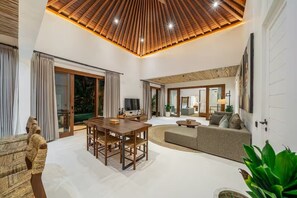 A spacious living area with a wooden ceiling, a dining table, a sofa, and a TV. - Harmony Villa by DH (Gianyar)