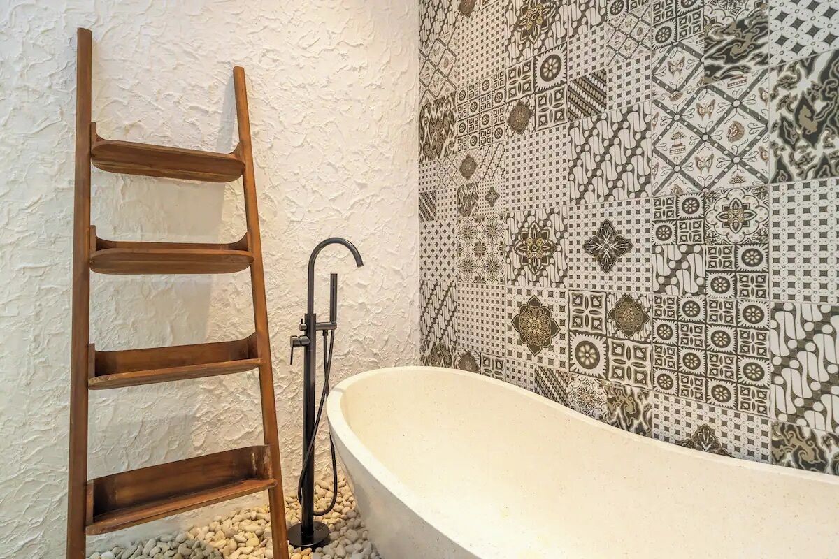 Een badkamer met een losstaand houten ladder, een badkuip en een betegelde muur met geometrische patronen.