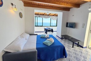 Ein Schlafzimmer mit Bett, Fernseher, Tisch und Meerblick.