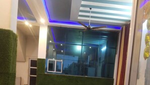 A modern interior with a large window, a ceiling fan, and a green artificial plant. - Hotel Deluxe And Family Resturant (Lachhmangarh)