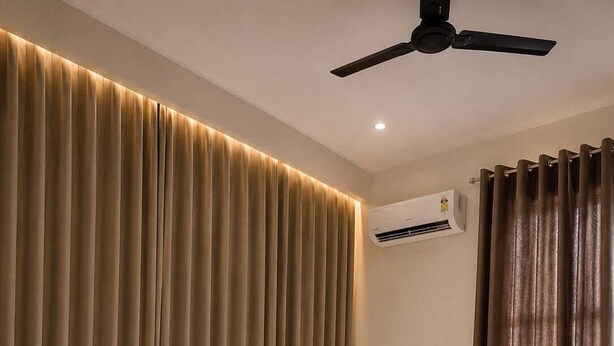 A modern bedroom with a bed, curtains, an air conditioning unit, and a ceiling fan. - Hotel Deluxe And Family Resturant (Lachhmangarh)