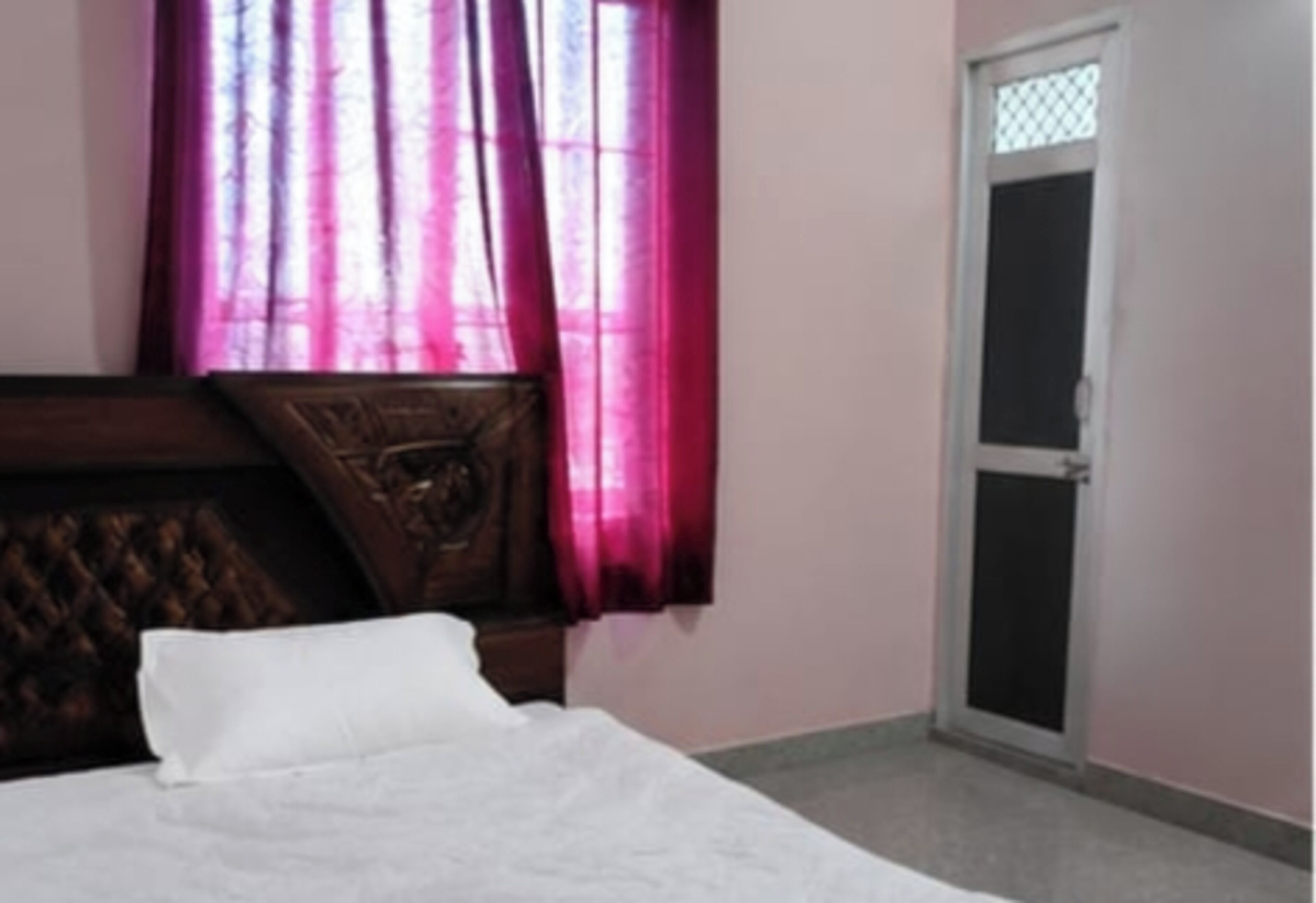 A bedroom with a bed, a window with curtains, a door, and a wall with a textured panel.