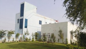 A modern building with a flat roof, a large window, and a swing set in the yard. - Hotel Deluxe And Family Resturant (Lachhmangarh)