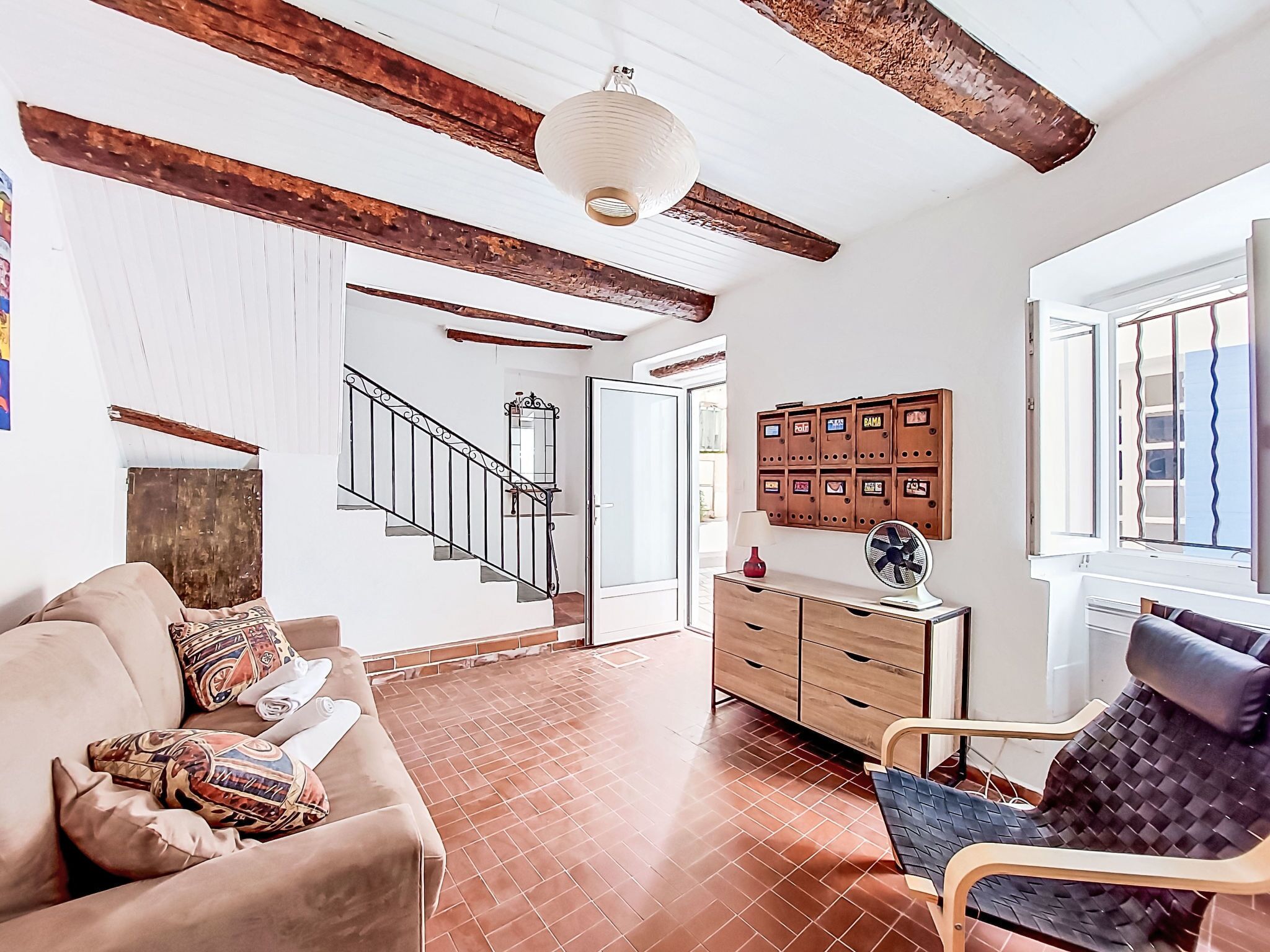 Een kamer met een houten trap, een bank, een stoel, een houten kast en een raam met jaloezieën.