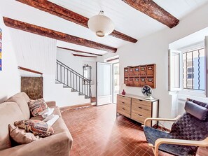 Una habitación con escalera de madera, un sofá, una silla, un armario de madera y una ventana con persianas.