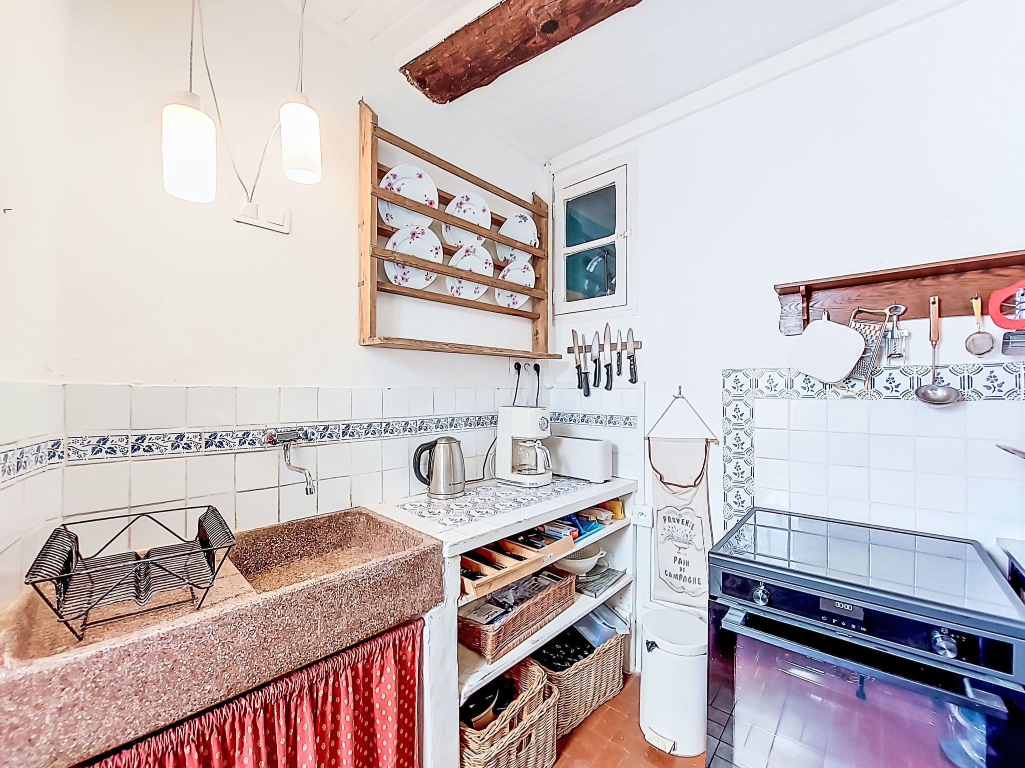 A kitchen with a countertop, a sink, a stove, and a hanging rack with kitchen utensils.