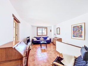 Una habitación con sofá, televisor, mesa de madera, silla, cómoda y un cuadro en la pared.