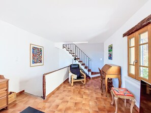Un escalier menant à un deuxième étage, un bureau en bois avec une chaise et une fenêtre donnant sur un paysage verdoyant.