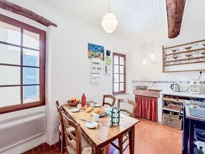 Eine Küche mit Esstisch, Stühlen, einer Hängelampe und einem Fenster mit Fensterläden.