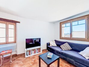 Ein Wohnzimmer mit Fernseher, Bücherregalen, einer Couch und einem Fenster.