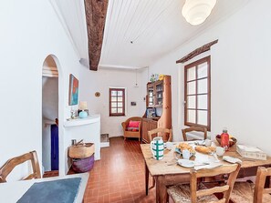 A dining area with a wooden table set for breakfast, a wicker chair, and a cabinet with glass doors. - Vacation home La Vue by Interhome (La Cadière d'Azur)