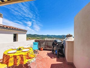Eine Terrasse im Freien mit Esstisch, Grill und Blick auf die Landschaft.