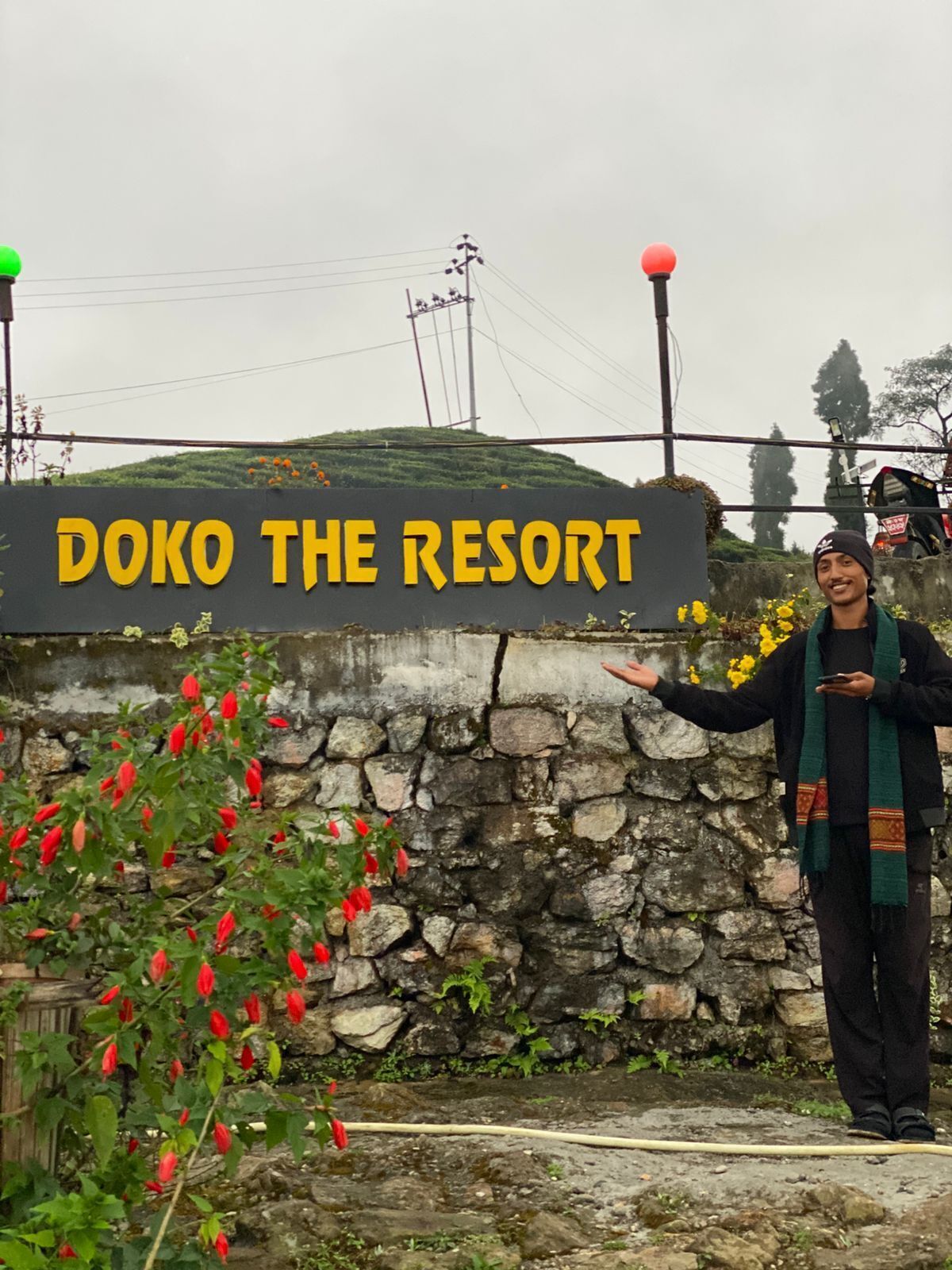 A sign for Doko The Resort with a stone wall and red flowers in the foreground.