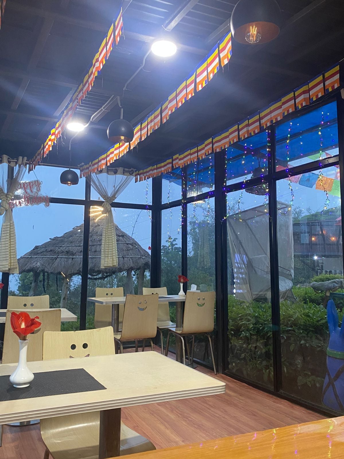 A restaurant with tables and chairs, a thatched-roof structure outside, and string lights.