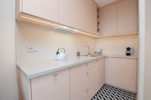 A modern kitchen with light-colored cabinets, a white countertop, a kettle, a coffee maker, and a patterned floor. - Bright Studio in Center | Close to the Beach | Balcony (Gdynia)