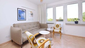Un soggiorno con divano, due poltrone, un tavolino, una ventola a soffitto e ampie finestre.