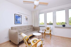 A living room with a sofa, two chairs, a small table, a ceiling fan, and large windows. - Bright Studio in Center | Close to the Beach | Balcony (Gdynia)