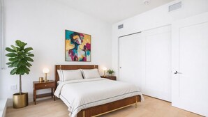 Ein Schlafzimmer mit einem Bett, Nachttischen, einer Topfpflanze und einem farbenfrohen abstrakten Gemälde an der Wand.