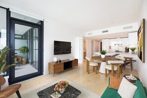 Ein modernes Wohnzimmer mit Fernseher, Sofa, Couchtisch und Essbereich.