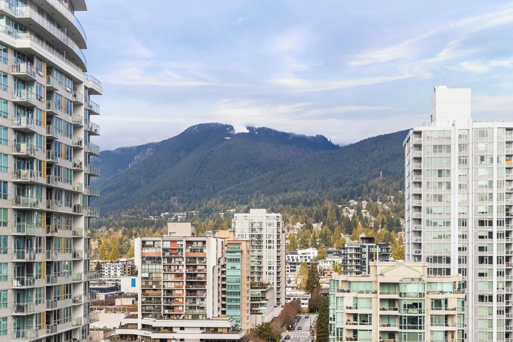 Une vue urbaine avec des immeubles modernes de grande hauteur, une montagne en arrière-plan et un ciel dégagé.