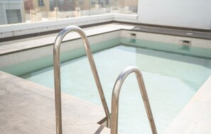 Ein Schwimmbecken mit Metallleitern, klarem Wasser und einer gefliesten Liegefläche.
