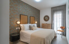 Ein Schlafzimmer mit Bett, Nachttischen, Kommode, Stuhl und Wand mit dekorativem Muster.