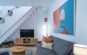 Ein modernes Wohnzimmer mit Treppe, einem Flachbildfernseher, einer Couch und einem großen abstrakten Gemälde.