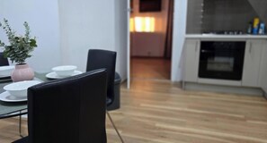 Spiseområde med et bord dækket til fire personer, en potteplante og et køkken i baggrunden.
