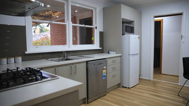 Una cocina moderna con estufa a gas, lavavajillas, refrigerador y ventana con vista a un muro de ladrillo.